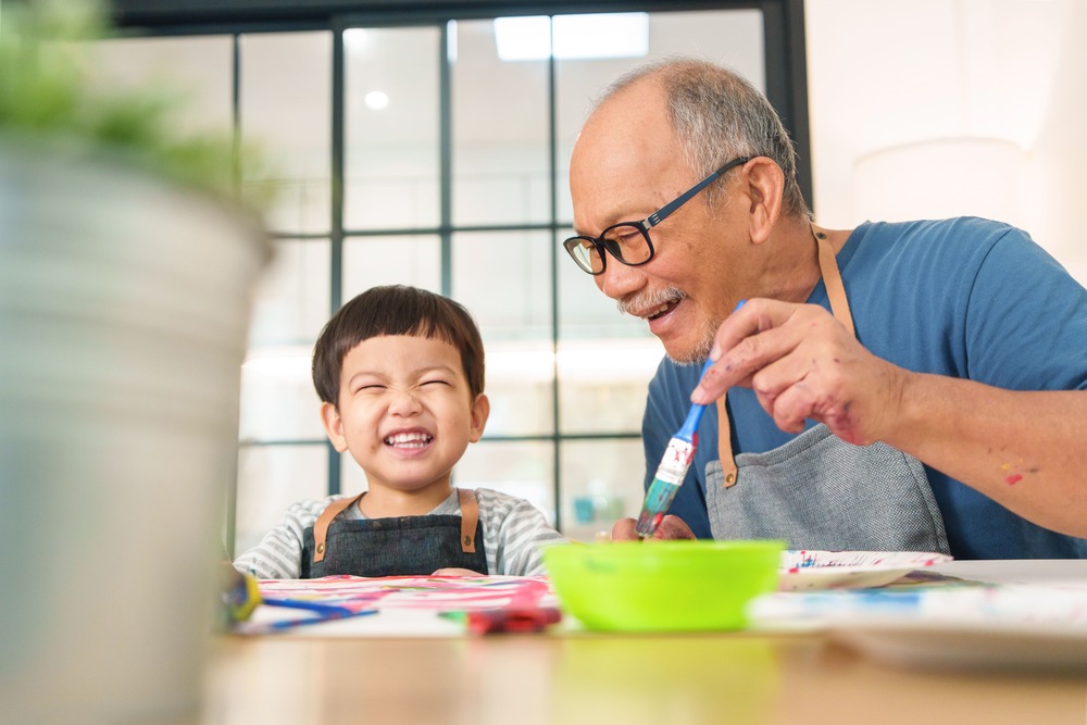 A grandfather and grandchild laughing while painting together